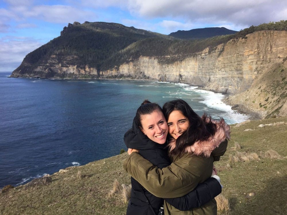 Amigos Australia dos chicas morena abrazándose y detrás el mar y las montañas